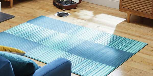 Image of striped blue rug on wooden floor next to blue armchair.